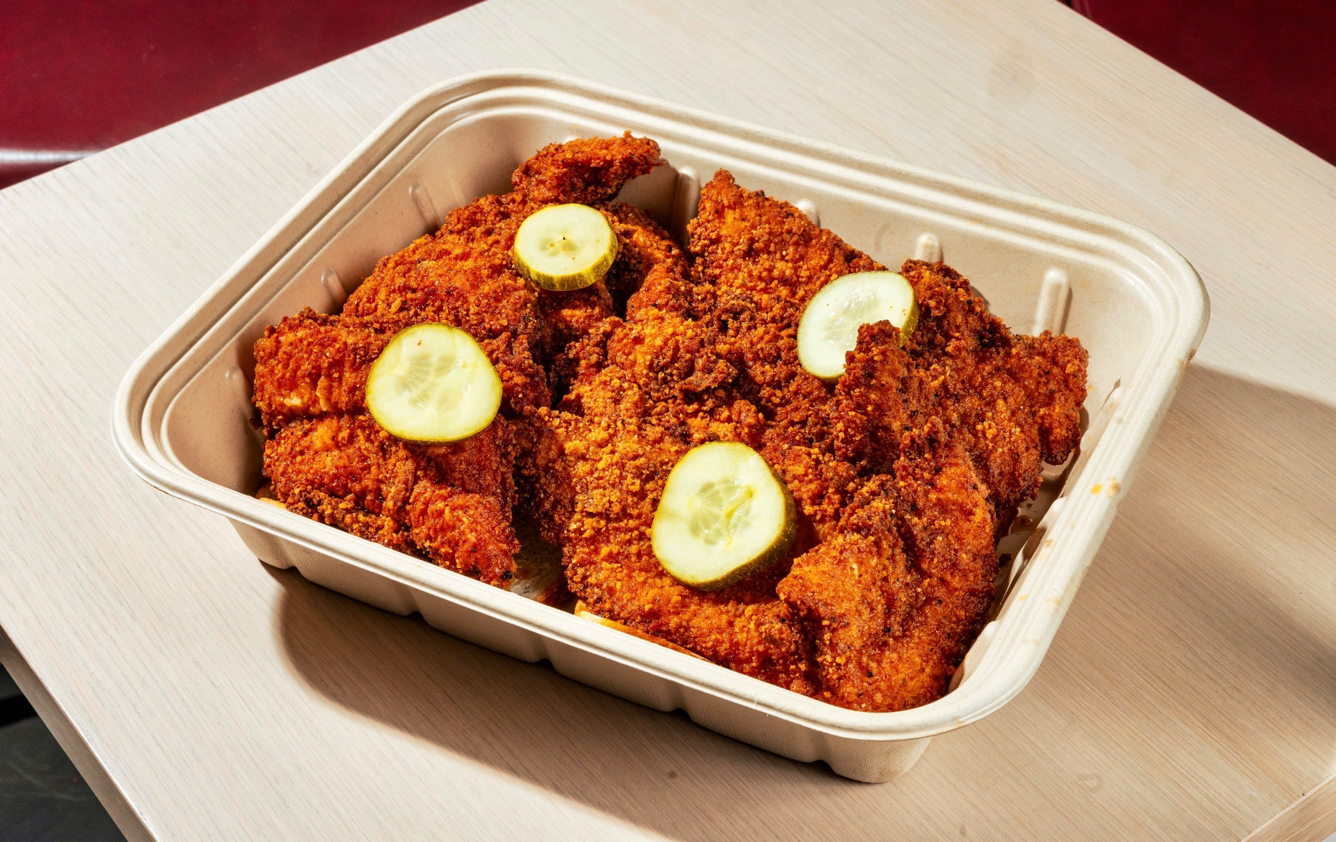 Fried chicken tenders in a tray topped with pickle chips